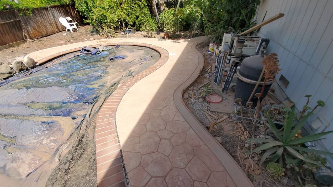 picture of a new concrete walkway surrounding a pool with custom pavers